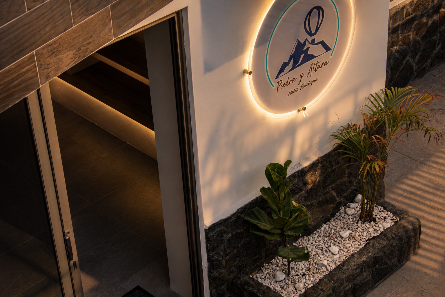Entrada principal con logotipo iluminado del Hotel Boutique Piedra y Altura